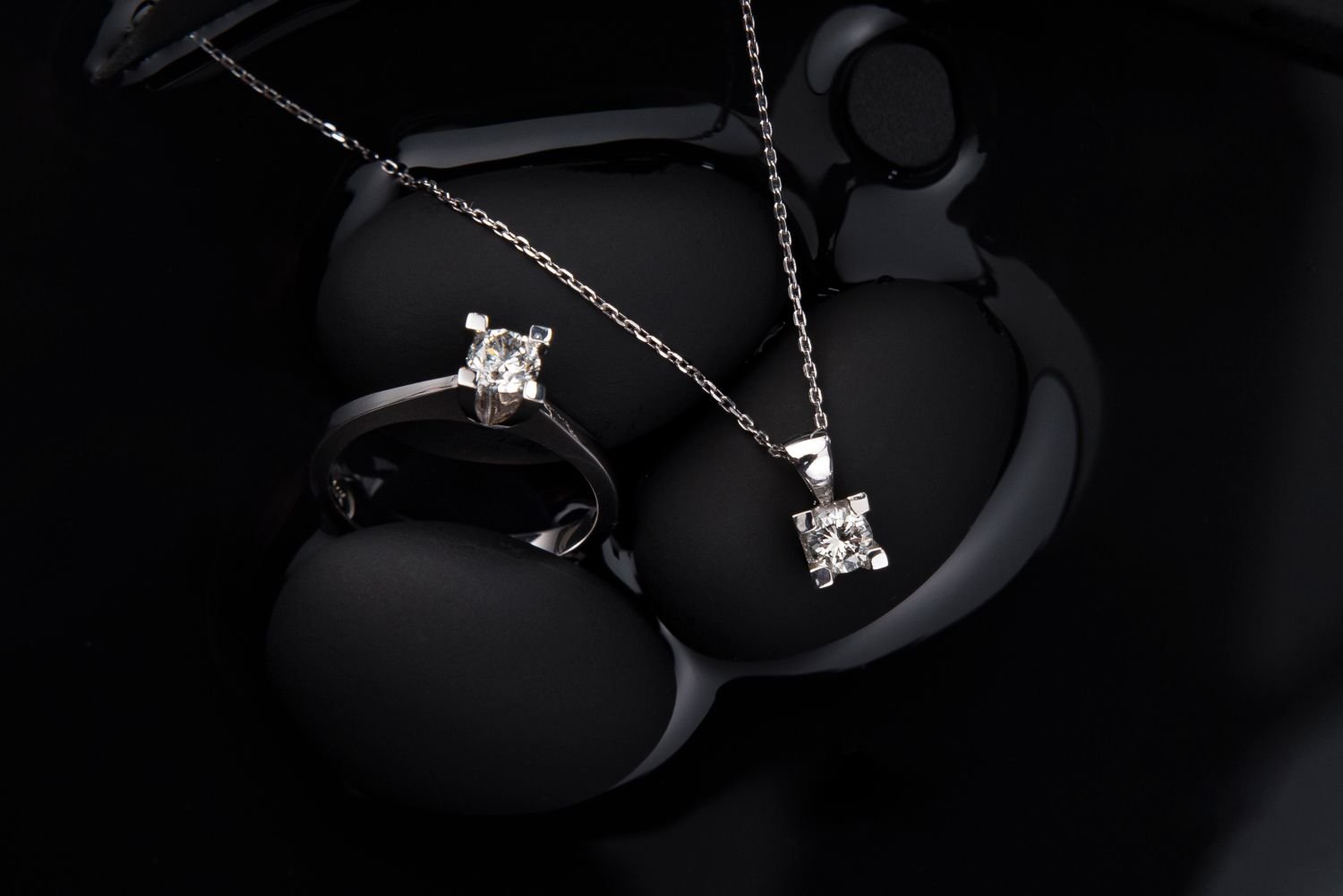 A lab-grown diamond solitaire ring and pendant on a dark reflective surface